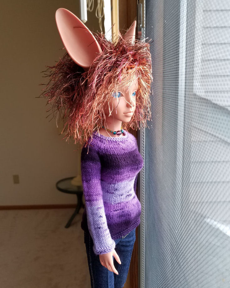 A fennec eared human doll in terracotta colored resin, Featherfall Iruhi, standing looking out the window. She is lit with natural light and is wearing a sweater striped in various shades of purple. The sleeve facing us fades from dark are the shoulder to pale at the cuff.